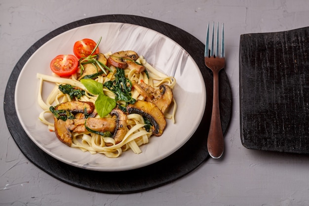 Udon met champignons en spinazie in een bord op een betonnen ondergrond bij een vork en een houten plank a