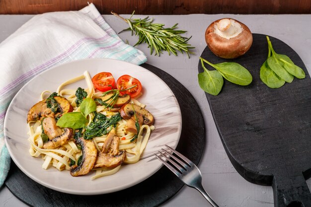 Udon met champignons en spinazie in een bord op een servet op een betonnen ondergrond in de buurt van greens en champignons op een zwart bord