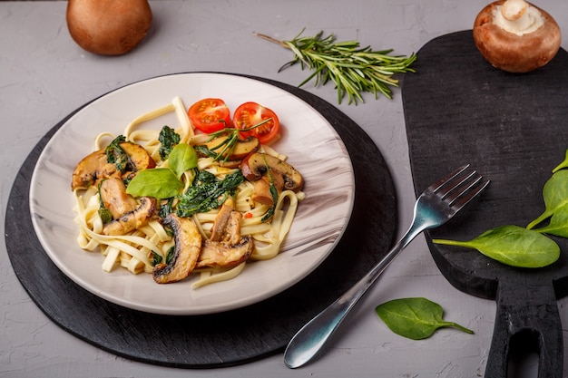 Udon met champignons en spinazie in een bord op een servet op een betonnen ondergrond in de buurt van greens en champignons op een zwart bord