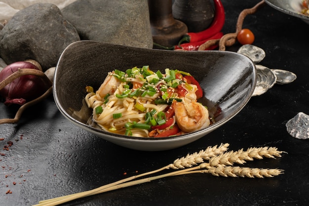 Udon noedels met garnalen en groene uien op een zwarte stenen keukentafel