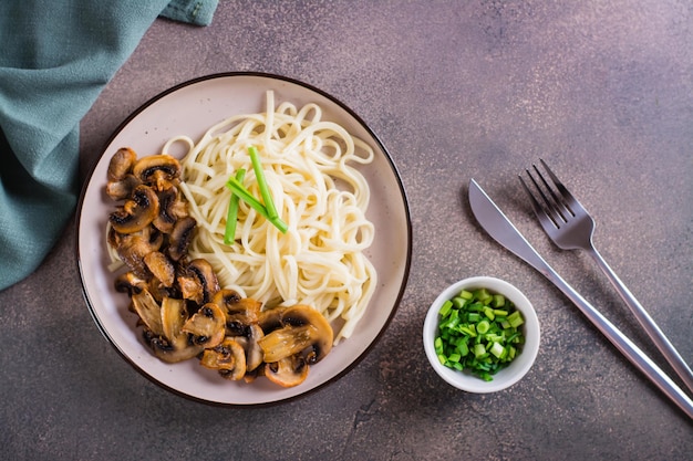 Udon noodles and fried mushrooms on a plate for homemade dinner top view