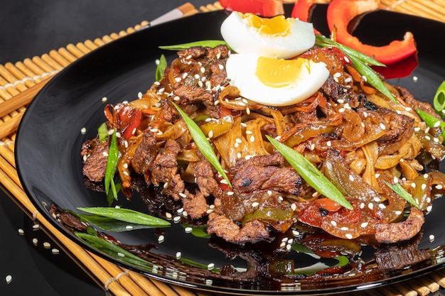 Udon noodles with meat mushrooms and vegetables Sprinkled with sesame seeds Asian food roast on black background