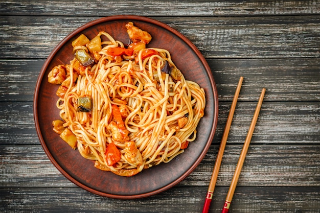 Udon-roerbakken noedels met kip en zoetzure saus en houten stokken op houten tafel