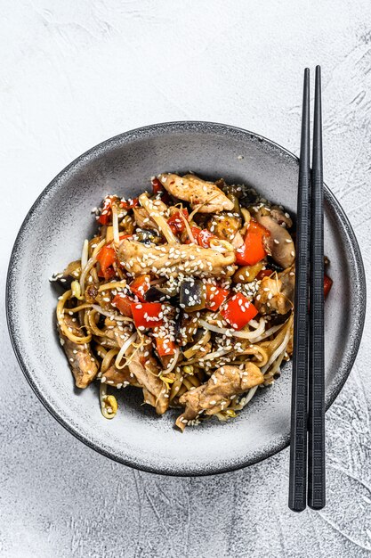 Udon roerbaknoedels met kippenvlees en sesam op grijs. Bovenaanzicht