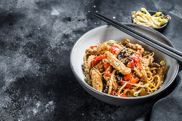 Udon roerbaknoedels met kippenvlees en sesam op zwart. Bovenaanzicht. Kopieer ruimte