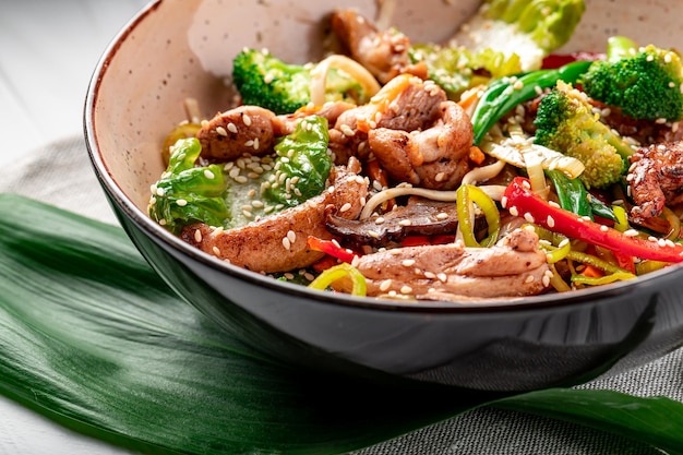 Udon roerbaknoedels met varkensvlees en groenten in een bord op witte houten ondergrond