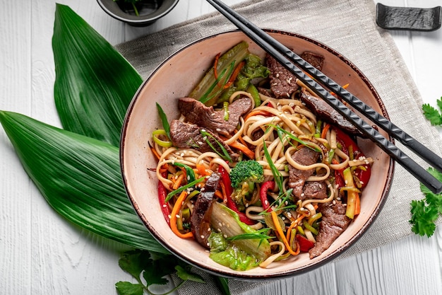 白い木製の背景に皿に牛肉と野菜を入れたうどん炒め麺