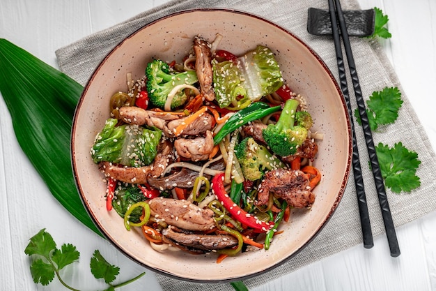 Udon friggere le tagliatelle con carne di maiale e verdure in un piatto su fondo di legno bianco