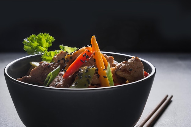 Лапша удон жареная со свининой и палочками для еды на черном каменном фоне азиатской кухни