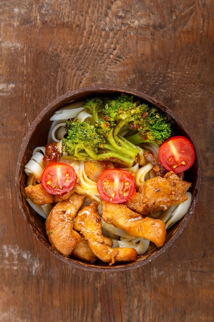 Udon with chicken in Japanese sauce on a plate of coconut shells on a wooden table Vertical