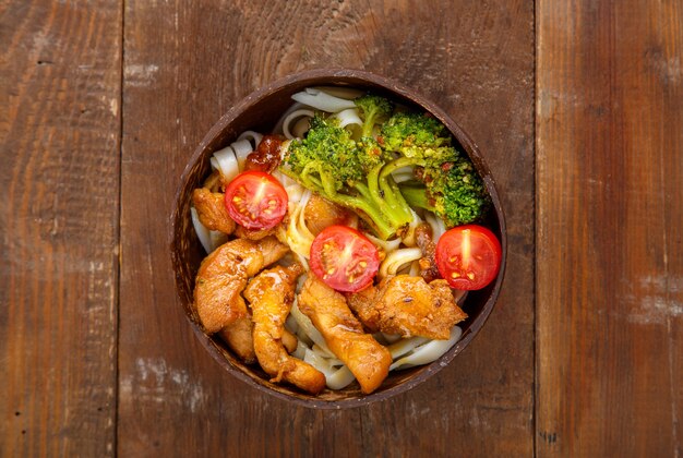 Udon with chicken in Japanese sauce and vegetables on a plate on a wooden table. Horizontal photo