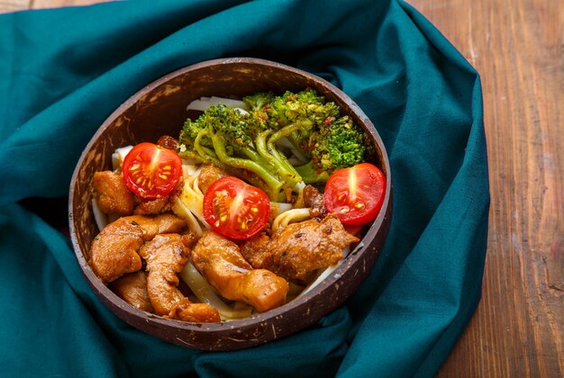 Udon with meat and vegetables in yakiniku sauce in a plate of coconut shells on a wooden table on a blue napkin. Horizontal photo