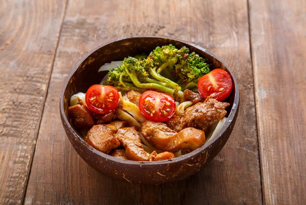 Udon with meat and vegetables in yakiniku sauce in a plate of coconut shells on a wooden table. Horizontal photo