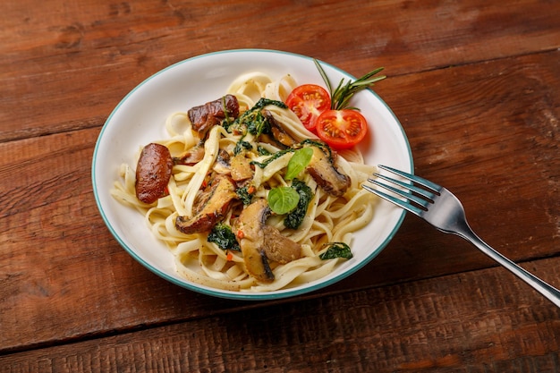 Udon with mushrooms and spinach and cherry tomatoes in a plate on a wooden table next to a fork