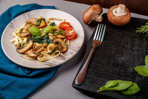 Udon with mushrooms and spinach in a plate on a blue napkin on a concrete background near mushrooms and cutlery on the board. Horizontal photo