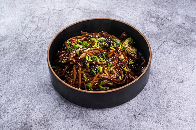 Photo udon with vegetables and sesame seeds on a gray background