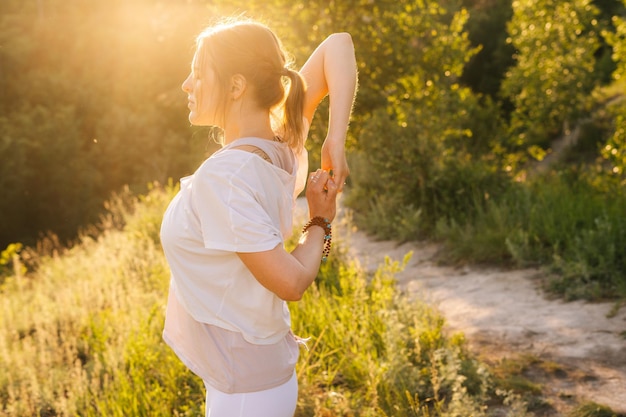 UFA RUSLAND 3 JUNI 2020 Jonge vrouw die Cow Face Pose buiten in parkavond oefent op achtergrond van zacht zonlicht zijaanzicht Portret van vrouw die complexe stretching yoga-oefening doet