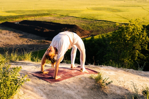 Photo ufa russia  3 june 2020 beautiful young woman practicing wheel yoga asana pose on top of rock background of beautiful landscape lady yogini doing yoga or pilates exercise bridge pose