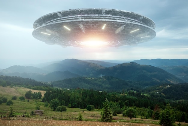 UFOエイリアンの受け皿が雲の中で山の上をホバリングし、空を静止してホバリングしている未確認飛行物体エイリアンの侵略地球外生命体旅行宇宙船