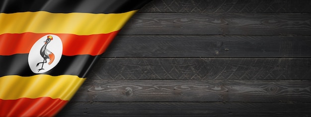 Uganda flag on black wood wall. Horizontal panoramic banner.