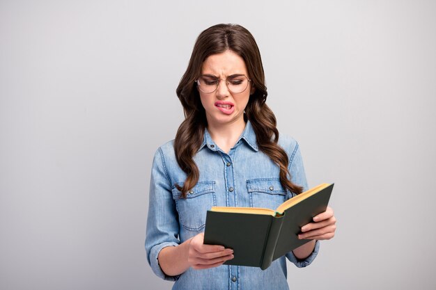 Ugh! Photo of pretty business lady hold book hands reader bad mood read disgusting chapter grinning wear specs casual jeans denim shirt isolated grey color