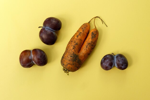 Ugly plums and carrot on yellow background fruits are suitable for food Concept Reduction of organic food waste