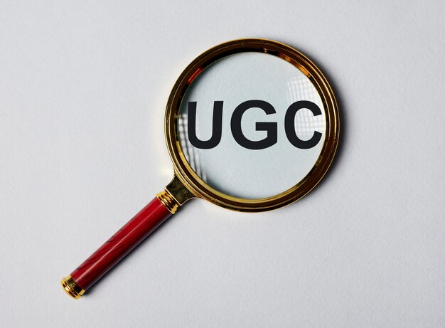 Ugs o acronimo di contenuto generato dall'utente per social media su superficie grigio blu con lente di ingrandimento.