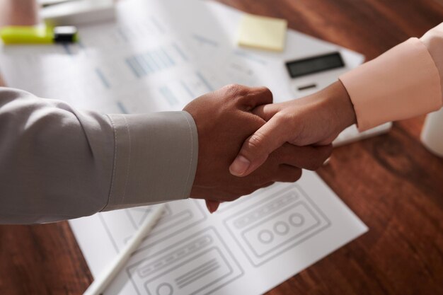 Ui designer and project manager shaking hands over table with mobile application mockups