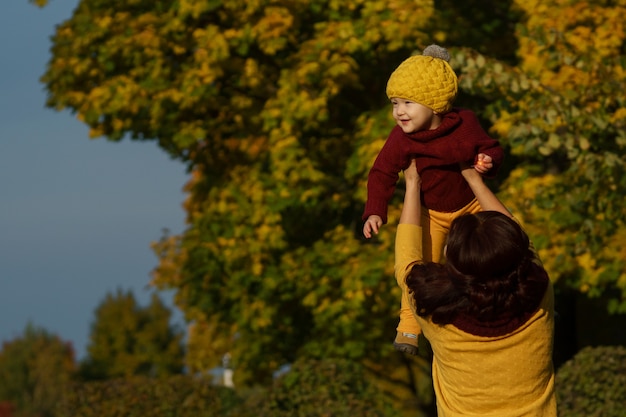 확인된 긍정적인 엄마는 따뜻하고 화창한 날 가을 공원을 산책하는 동안 작고 사랑스러운 딸을 던졌습니다