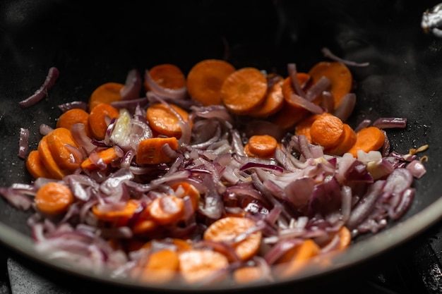 Uien en wortelen worden gebakken in een diepe koekenpan Voorbereiding voor het koken