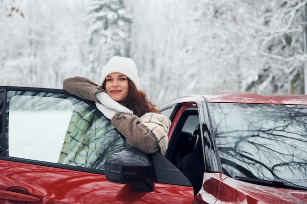 Uit de auto lopen Mooie jonge vrouw is in de winter buiten in de buurt van haar rode auto