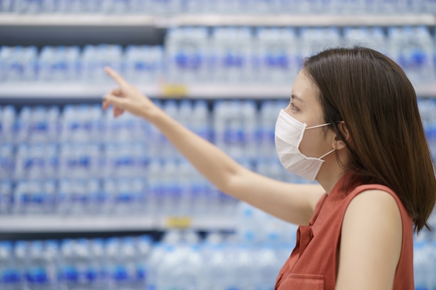 Uitbraak van Covid-19. Vrouw in medisch beschermend maskerpaniek het kopen drinkwater. Angst voor coronavirus.