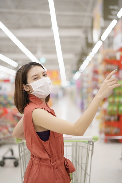 Uitbraak van Covid-19. Vrouw in medisch beschermend maskerpaniek het kopen voedsel. Angst voor coronavirus.