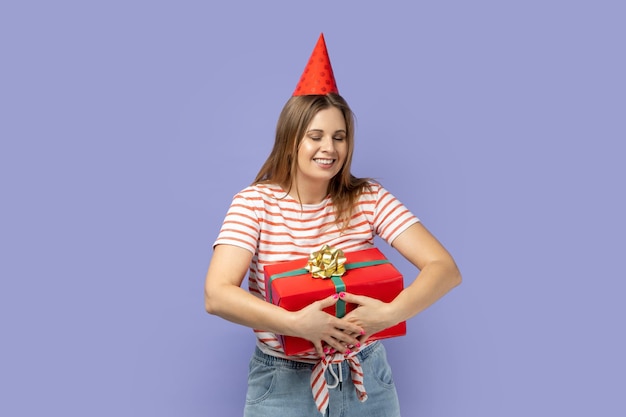 Uiterst gelukkige vrouw in feestkegel die de huidige doos omhelst en blij is om een coll-cadeau te krijgen