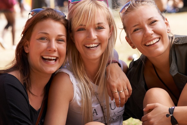 Uiteten met de meiden. Portret van drie lachende vrienden die arm in arm en op een festival zitten.