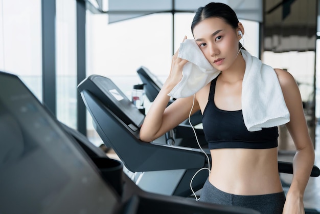 Uitgeput aziatisch vrouwelijk meisje dat op de loopband in de sportschool staat, ontspant en koelt gezond ideeënconcept af