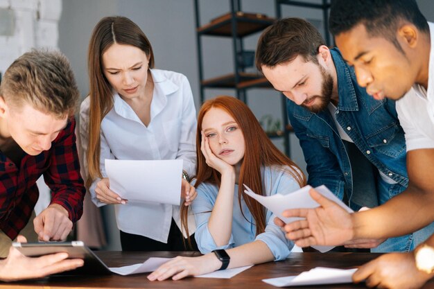 Uitgeput, vermoeide jonge zakenvrouw die aan bureaucollega's zit en documenten schudt?