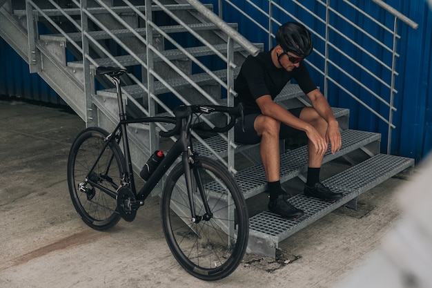 Uitgeputte fietser zittend op metalen trappen in de buurt van fiets buitenshuis