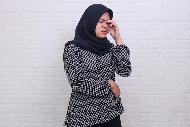 Uitgeputte jonge mooie Aziatische moslim die hijab draagt, zijn oog aanraakt met haar hand en moe voelt