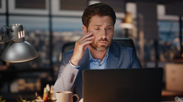 Uitgeputte man werkt op een laptop in een late nacht kantoor close-up vermoeide zakenman