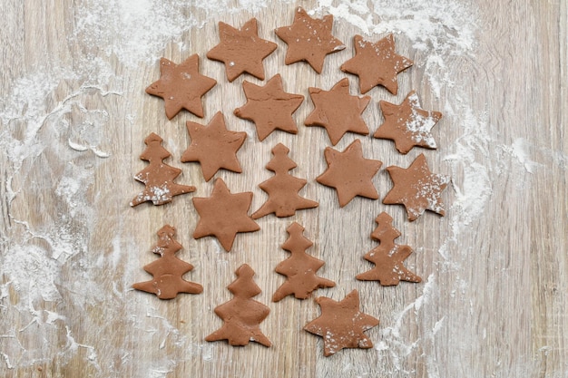 Uitgerold gekruid deeg gesneden in koekjessnijders op bakpapier op een houten tafel Kerst winter nieuwjaar Firtrees sterren meel