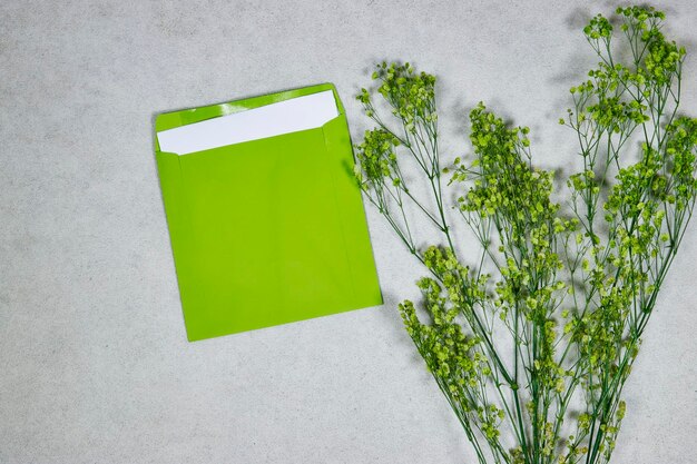 Uitnodiging of wenskaart mockup met verse groene gypsophila en envelop op grunge grijze pagina