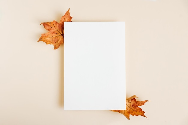 Uitnodigingskaart mockup met herfst esdoorn bladeren op beige pastel achtergrond sjabloon blanco wit papier mock up voor branding en reclame bovenaanzicht plat lag kopie ruimte