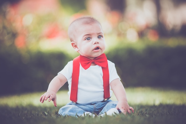 Uitstekende babyjongen met rode suspender in openlucht