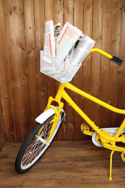 Uitstekende gele fiets met krant en pakket op houten muurachtergrond