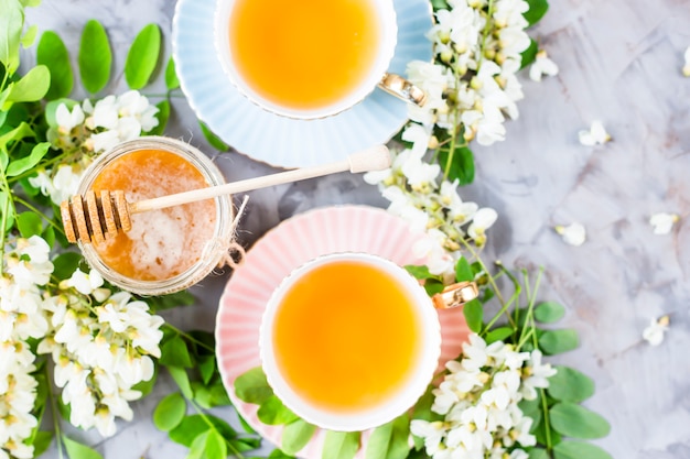 Uitstekende koppen met thee naast een kruik honing en acacia op een grijze lijst