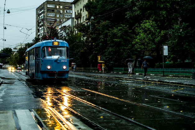 Uitstekende stadstram die zich in de straat tijdens de regen in de avond beweegt