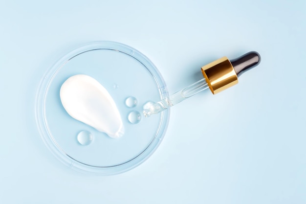 Uitstrijkje van crème slag en ronde transparante druppel gel serum in een petrischaal op een blauwe achtergrond Concept laboratoriumtests en onderzoek maken en testen van cosmetica