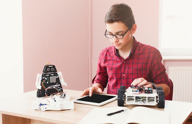 Uitvindingen en creativiteit voor kinderen. Geconcentreerde jongen programmeerrobot in het lab, met behulp van zijn digitale tablet. Gadgets, E-learning, moderne onderwijstechnologie, STEM-onderwijs.