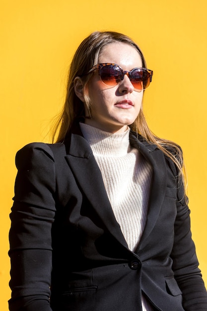 Uitvoerend ondernemer vrouw met zwarte jas en wollen trui en zonnebril op gele achtergrond in de straat met kopieerruimte Ondernemer vrouw concept